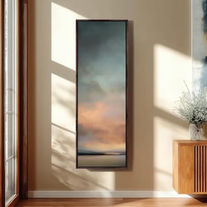 Könnte beinhalten: Ein hohes, vertikales, rechteckiges Wandbild mit einer Landschaftsmalerei bei Sonnenuntergang oder Sonnenaufgang. Das Kunstwerk zeigt weiche, verlaufende Farbübergänge in Dunkelblau, Grau und warmen Pfirsichtönen, gerahmt in einem dünnen, dunkelbraunen Holzrahmen.