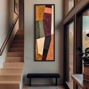 Op de afbeelding: Een hoog, rechthoekig ingelijst kunstwerk aan de muur met een abstracte compositie van geometrische vormen in tinten mosterdgeel, diep pruim, gedempt olijfgroen, crème, zwart en terracotta oranje, gevat in een dunne zwarte lijst.