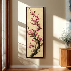 May include: A framed vertical canvas art piece featuring a blossoming tree branch with pink flowers. The artwork has a dark brown frame and is set against a cream-colored background. The tree trunk is dark brown, and the flowers are a vibrant pink.