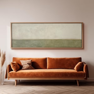 Op de afbeelding: Een rechthoekig ingelijst kunstwerk aan de muur met een horizontaal verdeelde compositie, bestaande uit een getextureerd gebroken wit bovengedeelte en een saliegroen ondergedeelte, geplaatst boven een bank van roestoranje fluweel.
