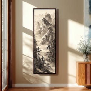 May include: A framed landscape painting showing a misty mountain scene in grey and sepia tones. The artwork features tall, jagged peaks, evergreen trees, and a sense of depth created by the fog. The painting is displayed on a beige wall.