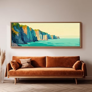 May include: A panoramic landscape painting in a light wood frame depicting steep coastal cliffs in shades of blue, green, and orange overlooking a turquoise sea under a pale yellow sky, mounted above a long, velvet-upholstered orange sofa.