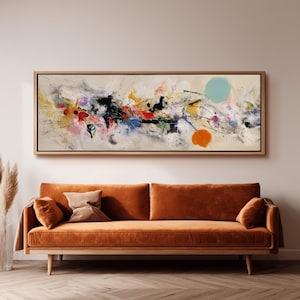 以下が含まれることがあります： 木製のフレームに入った抽象芸術絵画。作品は、黒、赤、黄、青、紫のペンキの飛沫があるクリーム色の背景が特徴です。オレンジ色とターコイズ色の2つの大きな円も存在します。絵画はオレンジ色のベルベットのソファの上に掛けられています。