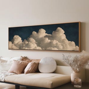 May include: A long, rectangular wall art piece featuring a detailed depiction of voluminous, off-white cumulus clouds set against a deep, dark navy blue sky. The artwork is encased in a thin, light-toned wooden frame, creating a horizontal display.