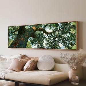 May include: A rectangular landscape painting in a light wood frame depicting a large tree trunk extending into a dense canopy of green leaves. The artwork uses a pointillist style with small dots of color to create the foliage and sky.