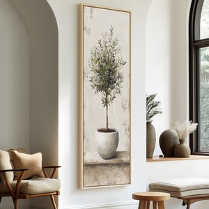 Op de afbeelding: Een hoog, verticaal rechthoekig wandkunstwerk met een schilderij van een olijfboom in een pot. De boom heeft een slanke stam en dicht groen blad, geplaatst in een afgeronde, lichtgekleurde keramische pot op een vlak, neutraal oppervlak.