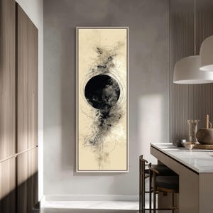May include: Abstract art print in a rectangular frame. The artwork features a large black circle with a cloud-like texture, surrounded by delicate lines and splatters on a cream-coloured background. The frame is white.