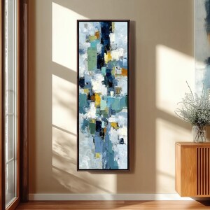 Può includere: Dipinto astratto verticale in formato rettangolare. L'opera d'arte presenta un mix di pennellate blu, gialle, verdi e bianche. Il dipinto è incorniciato in una cornice di legno marrone scuro ed è esposto su una parete beige.