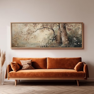 May include: A rectangular landscape painting in a light wood frame depicting a forest scene with large tree trunks, autumn-toned foliage, and soft light. The artwork is displayed above a long, solid burnt orange velvet sofa with matching cushions.
