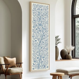 Puede incluir: Una impresión artística vertical enmarcada con un diseño de árbol azul sobre fondo crema. El árbol presenta intrincadas ramas y detalles florales. La obra de arte se muestra en un marco de madera clara, agregando un toque de elegancia a la decoración de la pared.