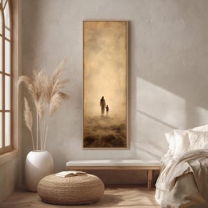 Puede incluir: Una impresión artística vertical enmarcada representa una silueta de un adulto y un niño caminando hacia una luz brillante. La obra de arte está en tonos sepia, con un fondo suave y brumoso. El marco es de color marrón claro. La impresión se exhibe en una habitación con tonos neutros.