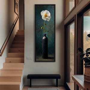 May include: A framed vertical canvas art piece featuring a white flower with a yellow center in a dark blue vase. The background is a dark teal with brushstrokes. The artwork is displayed above a black bench in a well-lit room with wooden stairs.