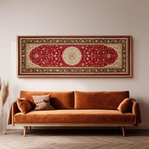 May include: A framed, rectangular red rug with an intricate floral design and a central medallion. The rug is framed in a light brown wooden frame and hangs above an orange sofa. The rug's border is black and gold.