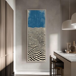 May include: Abstract art print featuring a black and white striped landscape design with a blue sky background. The artwork is framed in a white rectangular frame and hangs on a gray wall.