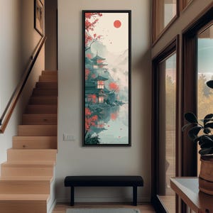 May include: A tall, vertical framed wall art print depicting a serene landscape with traditional multi-tiered pagodas nestled among misty mountains and red-leafed trees, reflected in a calm body of water under a solid red sun in a pale sky.
