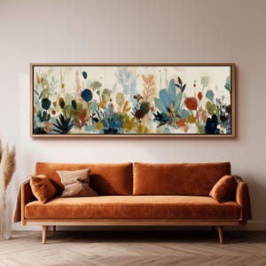 Peut inclure: Une peinture florale abstraite dans un cadre en bois est suspendue au-dessus d'un canapé en velours orange. L'œuvre présente une variété de plantes et de fleurs colorées dans des tons de bleu, vert, rouge et jaune sur un fond crème.