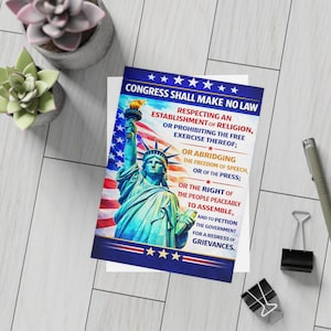 Può includere: Una stampa patriottica con la Statua della Libertà con la bandiera americana sullo sfondo. Il testo recita "Congress Shall Make No Law" seguito dal Primo Emendamento. La stampa è su una carta bianca.