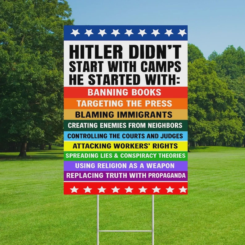 Puede incluir: Un letrero rectangular de jard&iacute;n con el texto "HITLER DIDN'T START WITH CAMPS HE STARTED WITH:" seguido de una lista de acciones en varios colores. El letrero est&aacute; sobre una estaca de metal, en una zona de c&eacute;sped con &aacute;rboles al fondo.