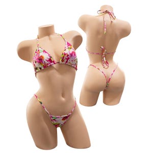 May include: A floral print bikini set displayed on a mannequin. The bikini top is a triangle style with halter straps. The bottoms are a thong style. The print features pink, white, and green flowers on a light background.