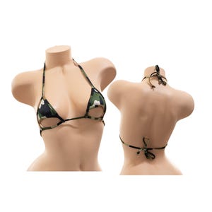 Puede incluir: Top de bikini con estampado de camuflaje con cuello halter y cierre de lazo. El top de bikini presenta un patrón verde, negro y beige. El top se muestra en un maniquí.