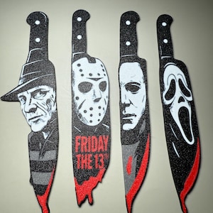 May include: Four decorative knife-shaped cutouts featuring horror movie characters. Each black cutout has a red blade and a character's face, including Freddy Krueger, Jason Voorhees, Michael Myers, and the Ghostface killer.