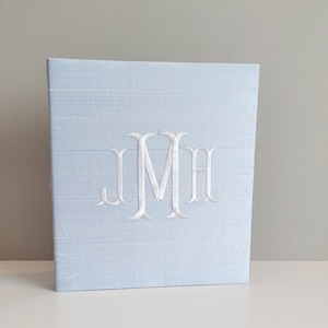 May include: A light blue fabric covered box with a white embroidered monogram "JMH" on the front.