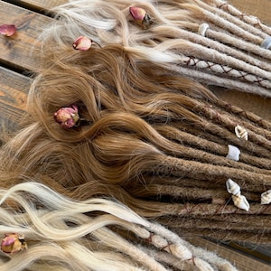 May include: An assortment of hair extensions in shades of blonde, light brown, and dark brown, with several dreadlock extensions. The extensions are arranged on a wooden surface and decorated with dried rosebuds and petals.