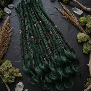 May include: Dark green dreadlocks with copper-colored accents and decorative braids. The dreadlocks are arranged on a dark surface, surrounded by moss, crystals, and dried plants. The dreadlocks have a natural, handmade appearance.