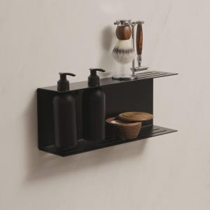 Könnte beinhalten: Ein schwarzes Metallregal mit zwei Ebenen, das schwarze Pumpflaschen, einen Rasierpinsel, einen Rasierer und eine Holzschale mit Deckel enthält. Das Regal ist an einer weißen Wand befestigt und bietet eine minimalistische Badezimmerästhetik.