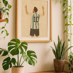 Puede incluir: Lámina enmarcada que presenta una ilustración estilizada de un futbolista con una camiseta a rayas azules y blancas con el número 10 en la espalda, con los brazos levantados. La obra está en un marco de madera, expuesta en una pared con plantas.
