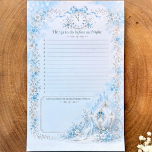 May include: A light blue notepad with a floral border and the text "Things to do before midnight." The notepad features a clock, a carriage, and a glass slipper illustration. The notepad has lined pages for notes.