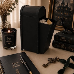 May include: A black arched storage box with a pull-out drawer, a black candle labeled Tales in the Shadows, a black notebook with the text FOCUS PLAN BLOOM, a black pen, a brass skeleton key, and two books titled POE TALES and DARK LEGENDS.