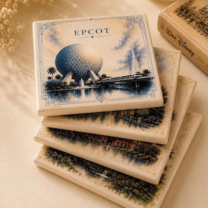 May include: A stack of four square ceramic coasters featuring illustrations of Epcot. The top coaster displays the Spaceship Earth geosphere, a monorail, and the text EPCOT in a blue and cream color palette with a decorative border design.