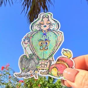 May include: A colorful sticker featuring a cartoon illustration of a woman with a heart-shaped design. The sticker has a green, pink, and gold color scheme with glitter accents. The woman is wearing a bow and has her eyes closed.