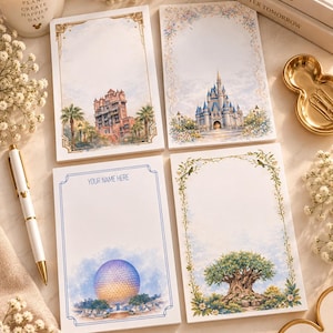 May include: Four rectangular paper notepads featuring watercolor illustrations of theme park landmarks including a hotel, a castle, a geodesic sphere, and a large tree. One notepad includes the printed text "YOUR NAME HERE" at the top.