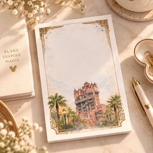 May include: A rectangular notepad featuring a watercolor illustration of the Hollywood Tower Hotel, surrounded by palm trees and a street lamp. The design includes a gold-toned art deco border on a light background, with clear text reading Hollywood Tower Hotel.