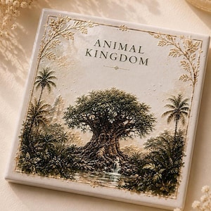 May include: A square ceramic tile featuring a raised, textured relief of a large tree and tropical foliage near a small waterfall. The text ANIMAL KINGDOM is printed in black at the top center. The border is decorated with gold-colored leaf motifs.