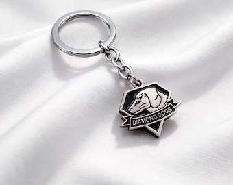 May include: Silver-toned keychain featuring a pendant with a dog's profile and the words "DIAMOND DOGS." The pendant is a geometric shape with a banner. The keychain has a circular ring and a chain.