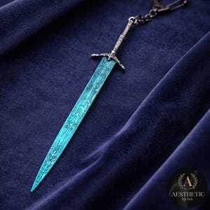 May include: A detailed, teal-colored sword keychain with an ornate handle and blade design. The blade has a unique pattern. The keychain is attached to a silver chain and is set against a dark blue background.