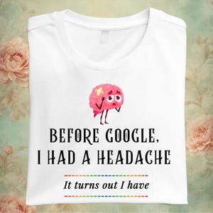 May include: White t-shirt with a graphic of a pink brain with a bandage and sad eyes. The text reads "BEFORE GOOGLE, I HAD A HEADACHE. It turns out I have" with a rainbow line below.