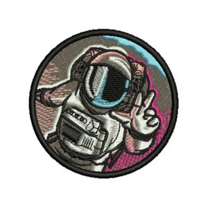 May include: Embroidered patch featuring an astronaut in a white spacesuit, giving a peace sign. The astronaut is inside a circular frame with a black border. The design includes pink, blue, and gray accents, creating a vibrant, cartoon-like aesthetic.