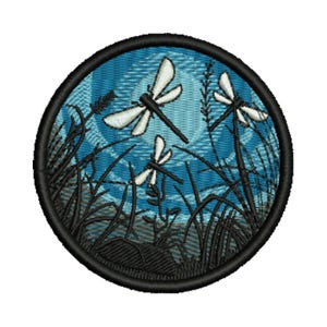 Può includere: Toppa ricamata raffigurante una scena naturalistica con tre libellule in volo su uno sfondo di cielo blu. Le libellule hanno ali bianche e corpi neri. Erba nera e canne in primo piano, con un bordo nero.