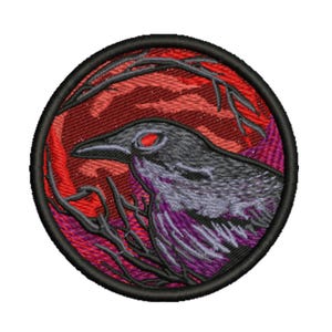 Puede incluir: Parche bordado circular que representa un cuervo estilizado con ojos rojos y detalles morados. El diseño incluye ramas oscuras sobre un fondo rojo y negro, todo dentro de un borde negro.