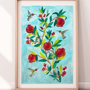 Puede incluir: Impresión artística enmarcada que presenta una ilustración de un árbol de granada con frutos rojos, hojas verdes y pequeñas flores rojas. Varios colibríes se representan volando alrededor del árbol sobre un fondo azul claro.