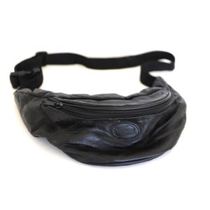 May include: Black leather fanny pack with a zippered main compartment and adjustable black strap. The bag has a rounded shape and a small embossed logo. A practical accessory for carrying essentials.