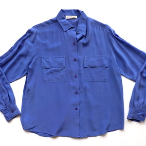 May include: A long-sleeved, button-down shirt in a vibrant blue hue. The shirt features a classic collar, two chest pockets, and buttoned cuffs. The fabric has a subtle sheen, suggesting a silk or satin material.