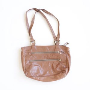 May include: A medium-sized brown leather shoulder bag featuring two horizontal zippered pockets on the front, a main top zipper closure, and two thin shoulder straps attached with silver-toned metal hardware connectors at the top.