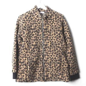 May include: A leopard print jacket in shades of tan and black, featuring a full-length zip. The jacket has black cuffs and is suspended from a white hanger. The garment is suitable for all and is set against a white backdrop.