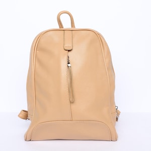 Puede incluir: Mochila de color beige con la parte superior redondeada y un asa pequeña. La mochila tiene una cremallera vertical con una lengüeta larga y dos cremalleras laterales. La bolsa es de material liso.