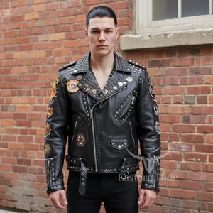 May include: Black leather jacket with silver studs and patches. The jacket has a notched collar, a zipper closure, and multiple pockets. Patches with various designs are sewn on the sleeves and chest. The jacket is worn with black pants.